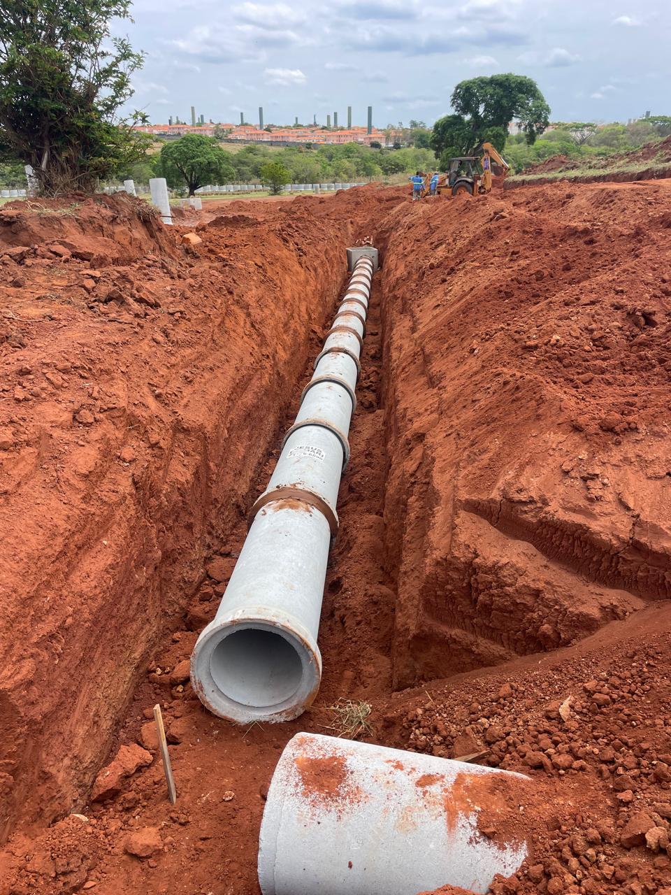Equipe e máquina posicionando tubulação de galeria pluvial